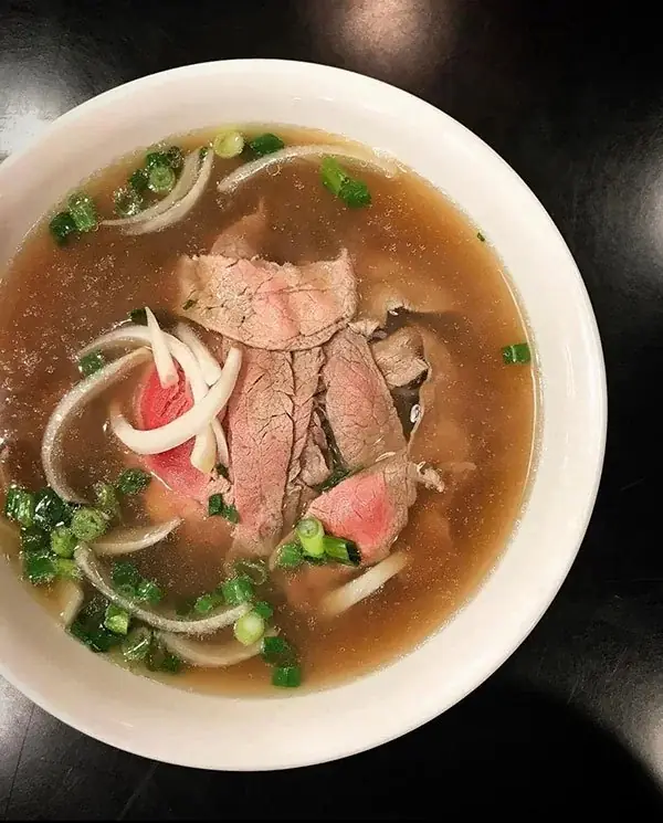 Bowl of beef pho with rare beef, onions and green onion in clear broth