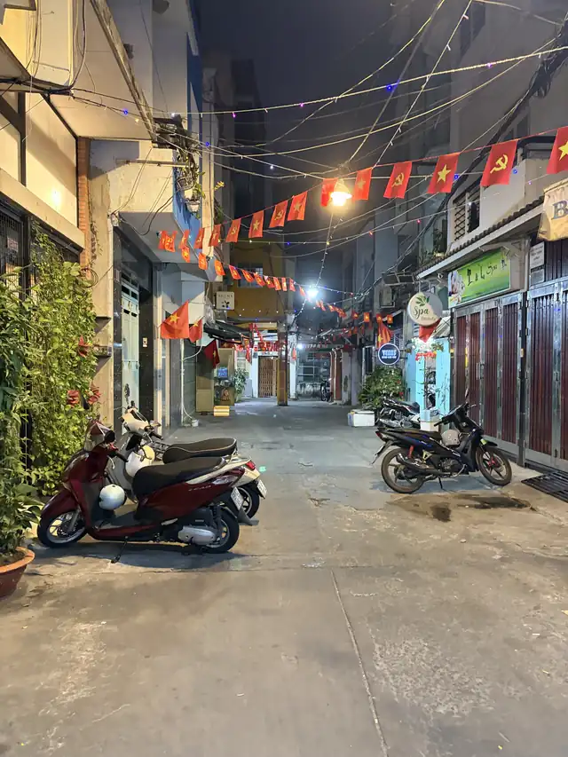 A narrow alley at night lined with parked scooters and strings of flags, where our family used to live