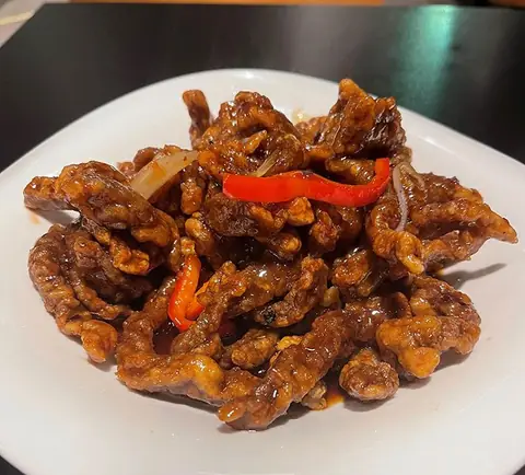 Real Ginger Beef: crispy glazed beef strips with red peppers on a white plate