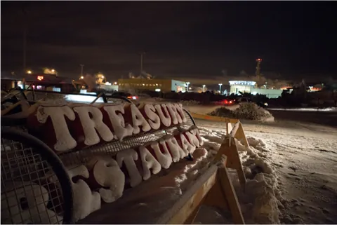 The snow-covered Treasury Restaurant sign lying behind wooden barricades at night after the fire