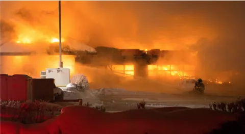 Treasury Restaurant in flames at night on December 25, 2012, with a firefighter spraying water through thick orange smoke